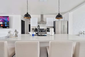 Een moderne keuken met een centraal eiland, roestvrijstalen apparatuur en hanglampen.