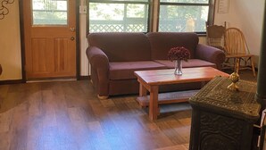 Una sala de estar acogedora con piso de madera, un sofá marrón, una mesa de centro de madera y un aparador decorativo.