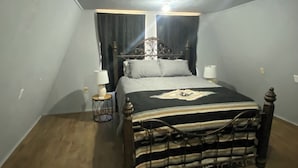 Un dormitorio con una cama, dos mesitas de noche, una lámpara en el techo y una ventana con cortinas.