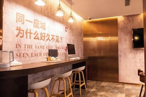 A hotel reception area with a modern design, featuring a reception desk, bar stools, a wall-mounted television, and a large text display. - Waiting Qingju Hotel (Shanghai New International Expo Center） (Shanghai)