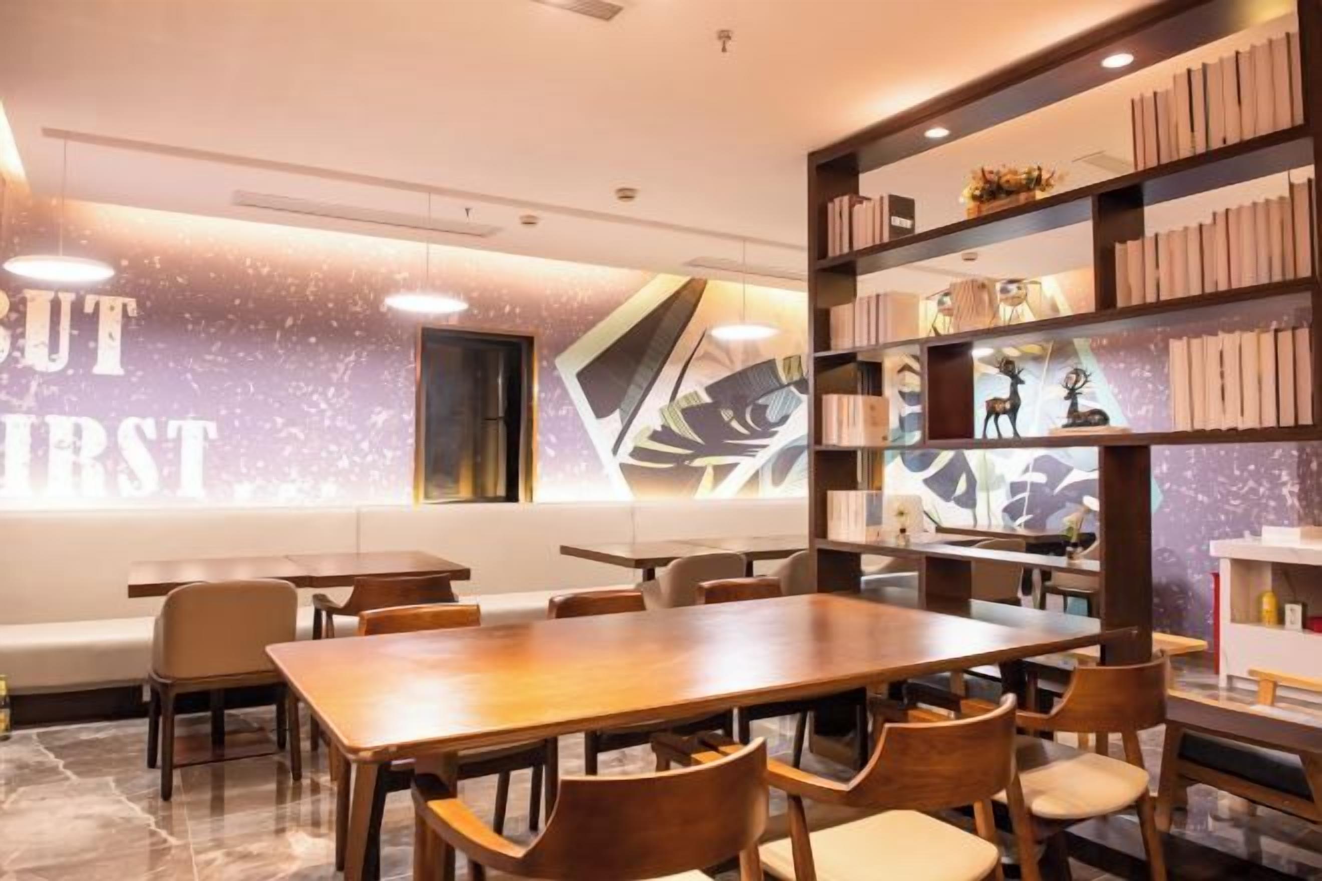 A modern interior with a long wooden table and chairs, a bookshelf, and a wall with a geometric design.