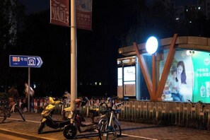 A street scene at night with a bus stop, bicycles, and a brightly lit advertisement. - Waiting Qingju Hotel (Shanghai New International Expo Center） (Shanghai)