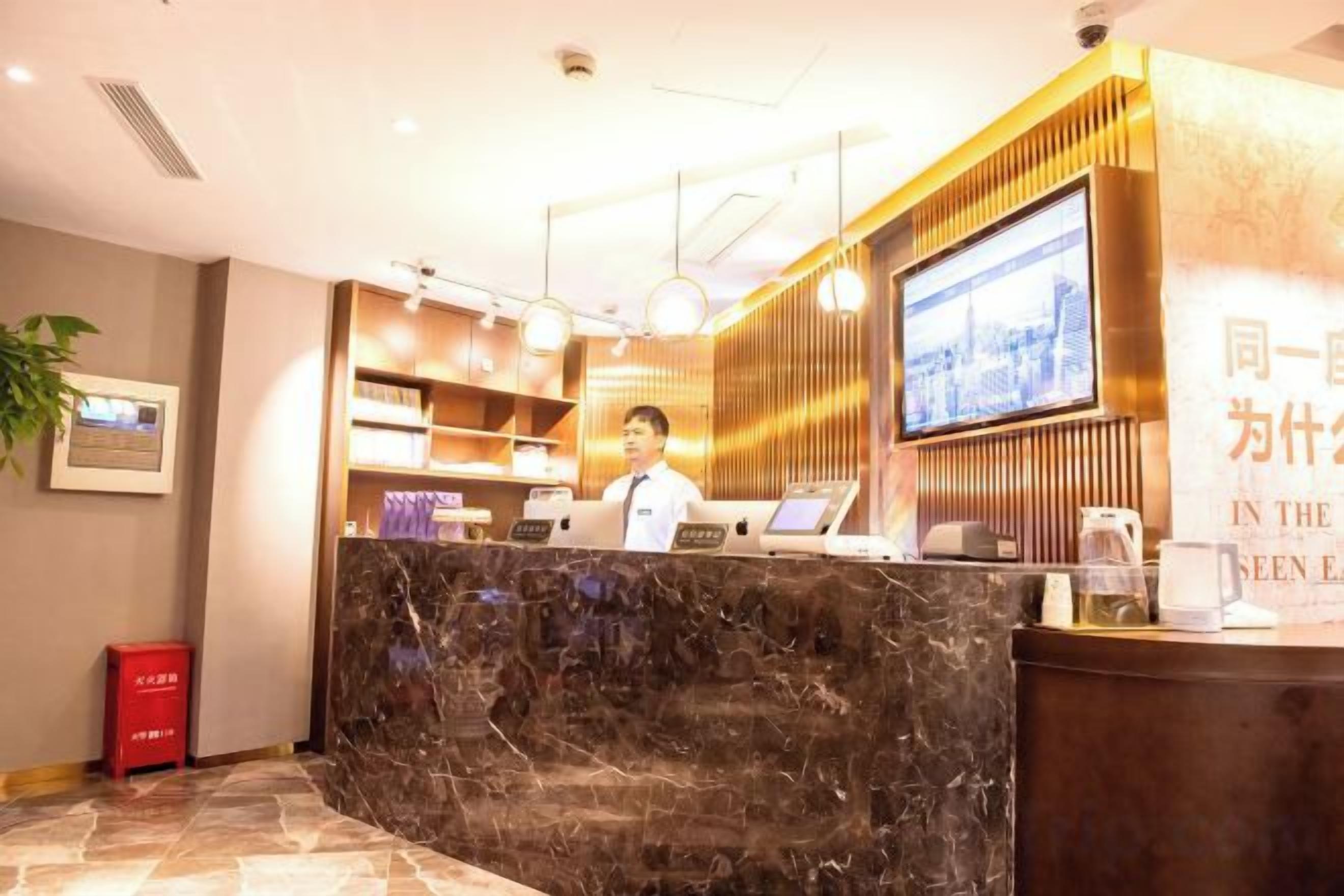 Zona de recepción de un hotel con mostrador de mármol, una pantalla de televisión y un recepcionista.