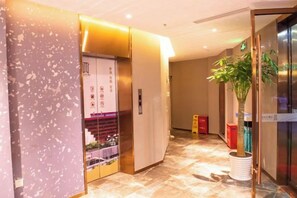 A hotel lobby with an elevator, a potted plant, and a tiled floor. - Waiting Qingju Hotel (Shanghai New International Expo Center） (Shanghai)