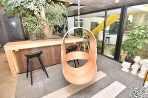 A modern interior with a wooden bar counter, hanging wooden chair, and potted plants. - Waiting Qingju Hotel (Shanghai New International Expo Center） (Shanghai)