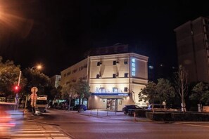 A multi-story building with illuminated signage, a visible entrance, and a street view with traffic lights and vehicles.