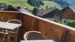 Eine Holzdachterrasse mit Tischen und Korbstühlen, mit Blick auf eine gebirgige Landschaft.