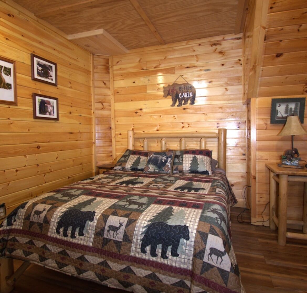 Een houten bed in een blokhut, een quilt met berenprint en een beren-vormig bord aan de muur.