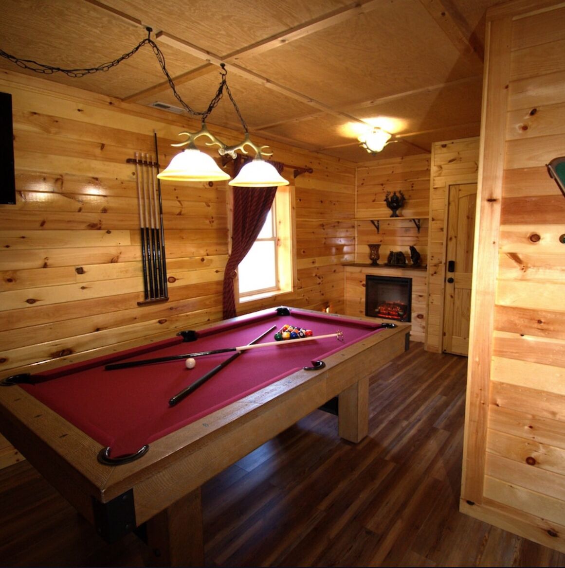 Una baita in legno con tavolo da biliardo, camino e lampadario.