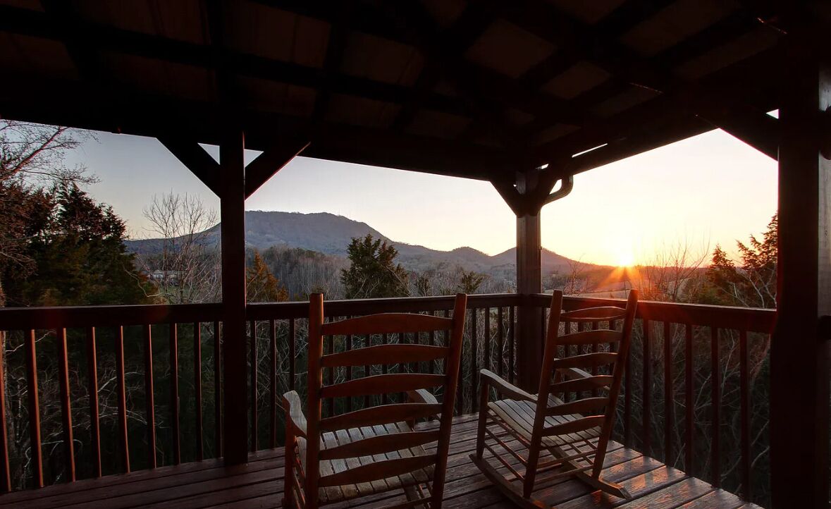 Une terrasse en bois avec deux fauteuils à bascule donnant sur un paysage montagneux au coucher du soleil.