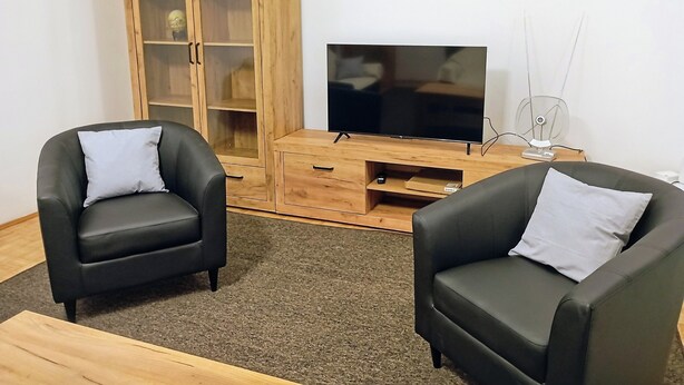 A living room with two black leather armchairs, a wooden cabinet with glass doors, and a flat-screen TV on a wooden stand. - Cozy Trogir Apartment With 3 Bedrooms (Trogir)