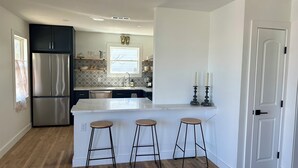 A modern kitchen with a stainless steel refrigerator, a white island with stools, and a window with a view.