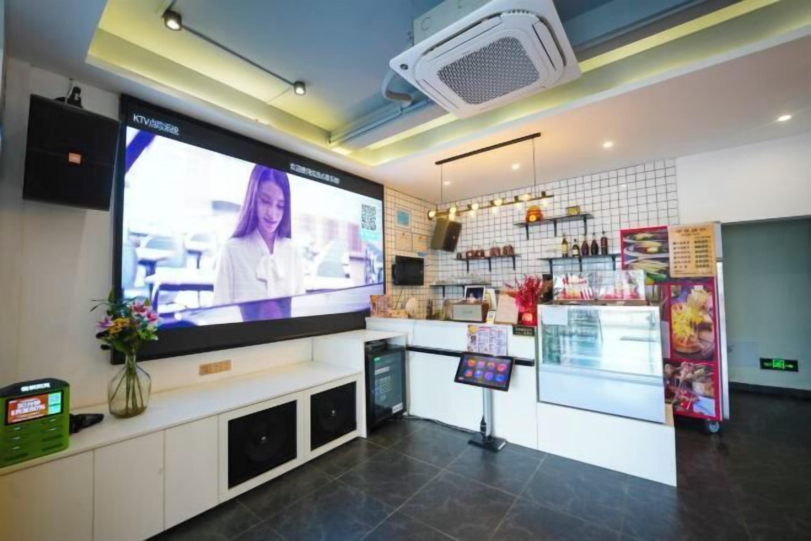 Hall d'albergo moderna con un grande schermo televisivo, una reception, un chiosco self-service e un'esposizione di cibi.