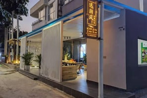A hotel entrance with a covered outdoor seating area, a signboard, and a door to the interior. - Seabreeze Inn (Shenzhen)