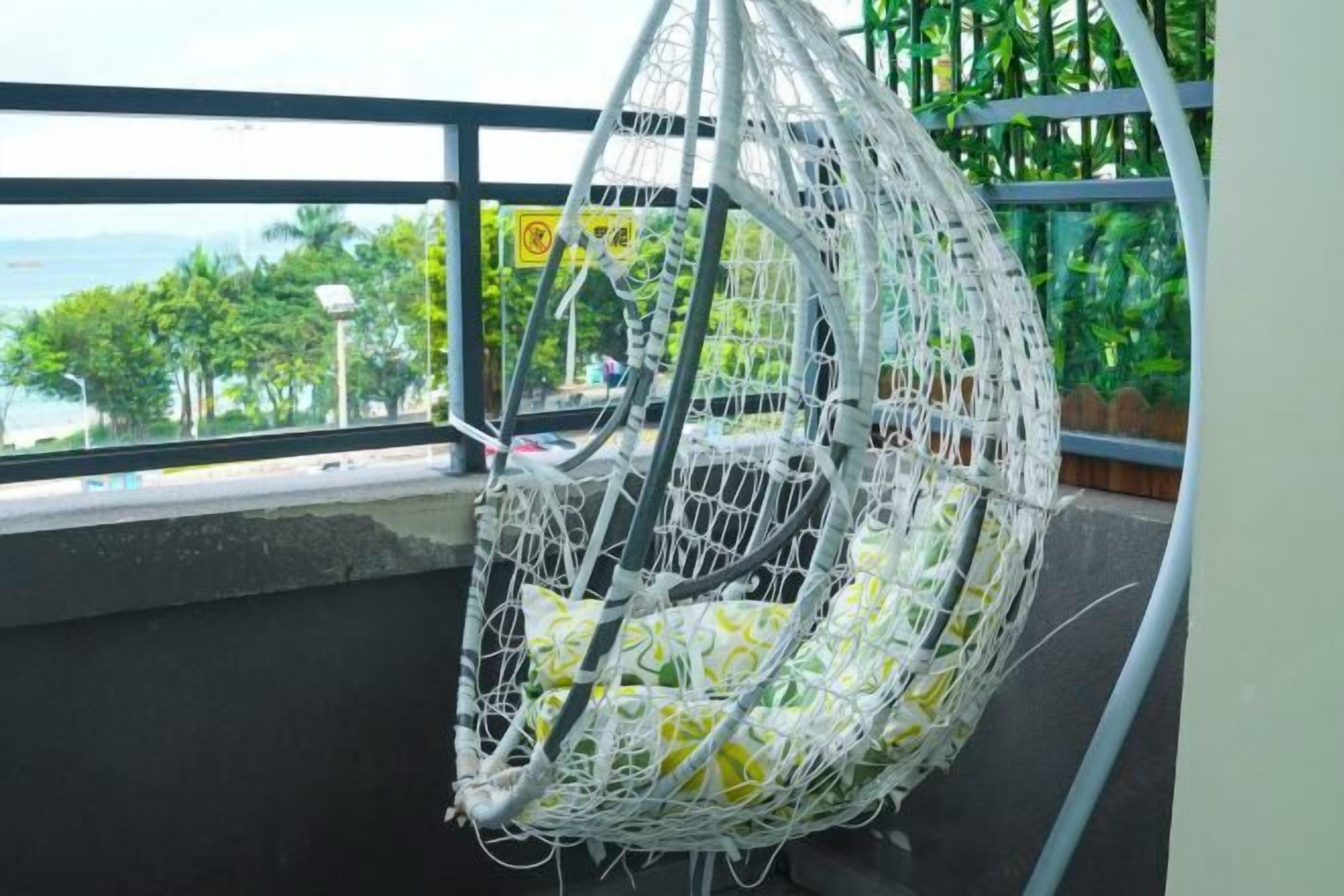 A white hanging chair with a cushion, positioned near a window overlooking a view of greenery and a body of water.