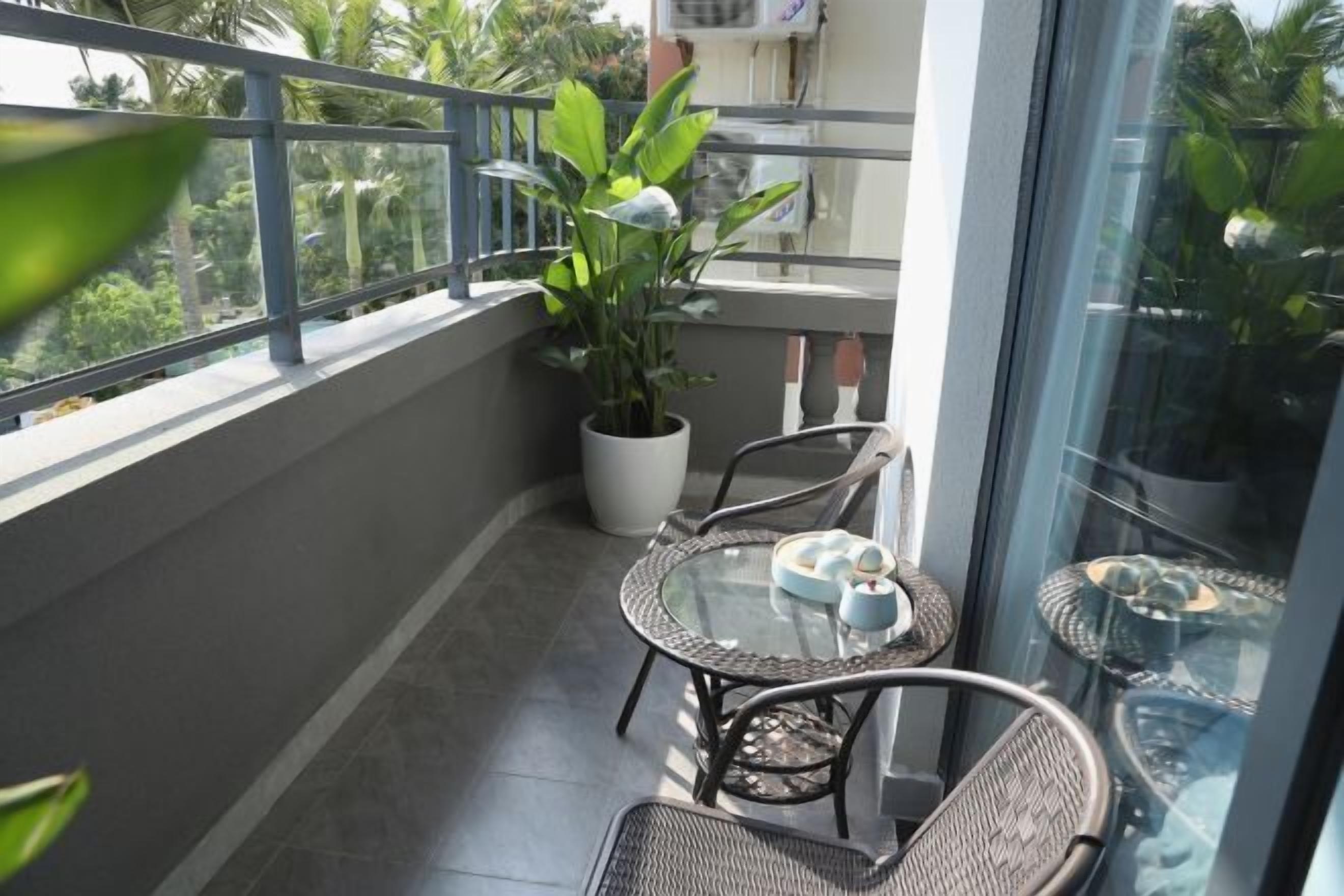 Un balcon avec une table et des chaises en verre, une plante en pot et une vue sur la verdure.