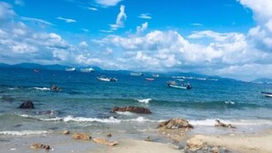 Ein Strand mit blauem Himmel, ruhigem Wasser und Booten in der Ferne.