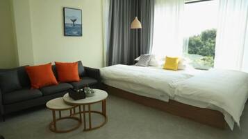 Quarto de hotel com cama, sofá, mesa pequena e janela com cortinas.
