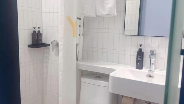 Un baño con pared de azulejos blancos, un lavamanos blanco, un espejo y una toalla colgada en la pared.