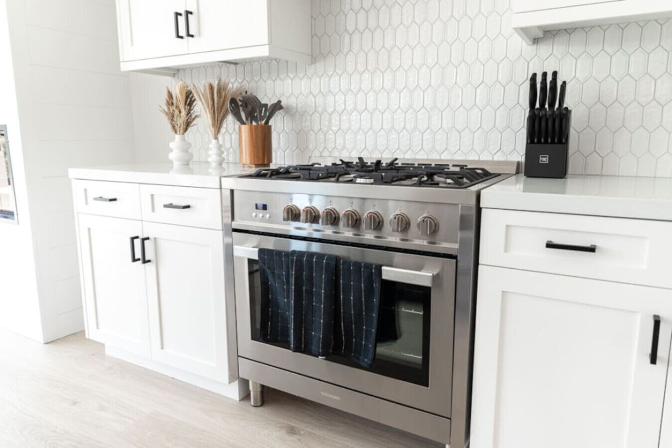 Una cocina moderna con gabinetes blancos, estufa de acero inoxidable y salpicadero de azulejos.