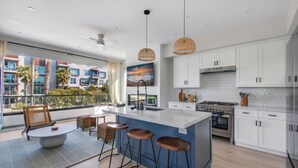 A modern kitchen with a large island, white cabinets, and a view of a residential area.