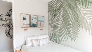 A bedroom with a bed, a wall with palm leaf artwork, and a door with a black and white octopus design.