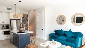 A modern kitchen with white cabinets, a blue island, and hanging wicker lights.