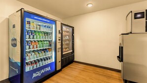 A room with a wooden floor, a refrigerator, and two vending machines labeled 'AQUAFINA'. - LivAway Suites Seattle-Renton (Renton)