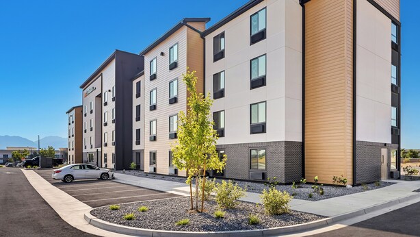 A modern multi-story residential building with a parking lot and a small landscaped area with trees. - LivAway Suites Seattle-Renton (Renton)