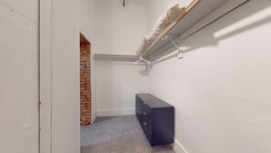 A narrow hallway with a brick wall, a white door, a black cabinet, and a white hanger on a wall-mounted rack.