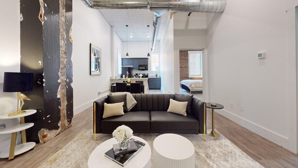 A modern living room with a dark sofa, a coffee table with books, and a kitchen in the background.
