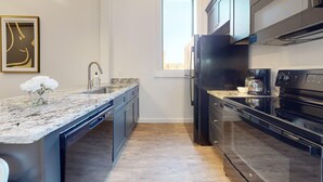 A modern kitchen with a granite countertop, stainless steel appliances, and a large window.