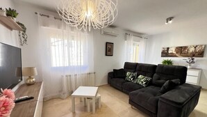 Una sala moderna con un sofá negro, una mesa de centro blanca y un televisor sobre un mueble de madera.