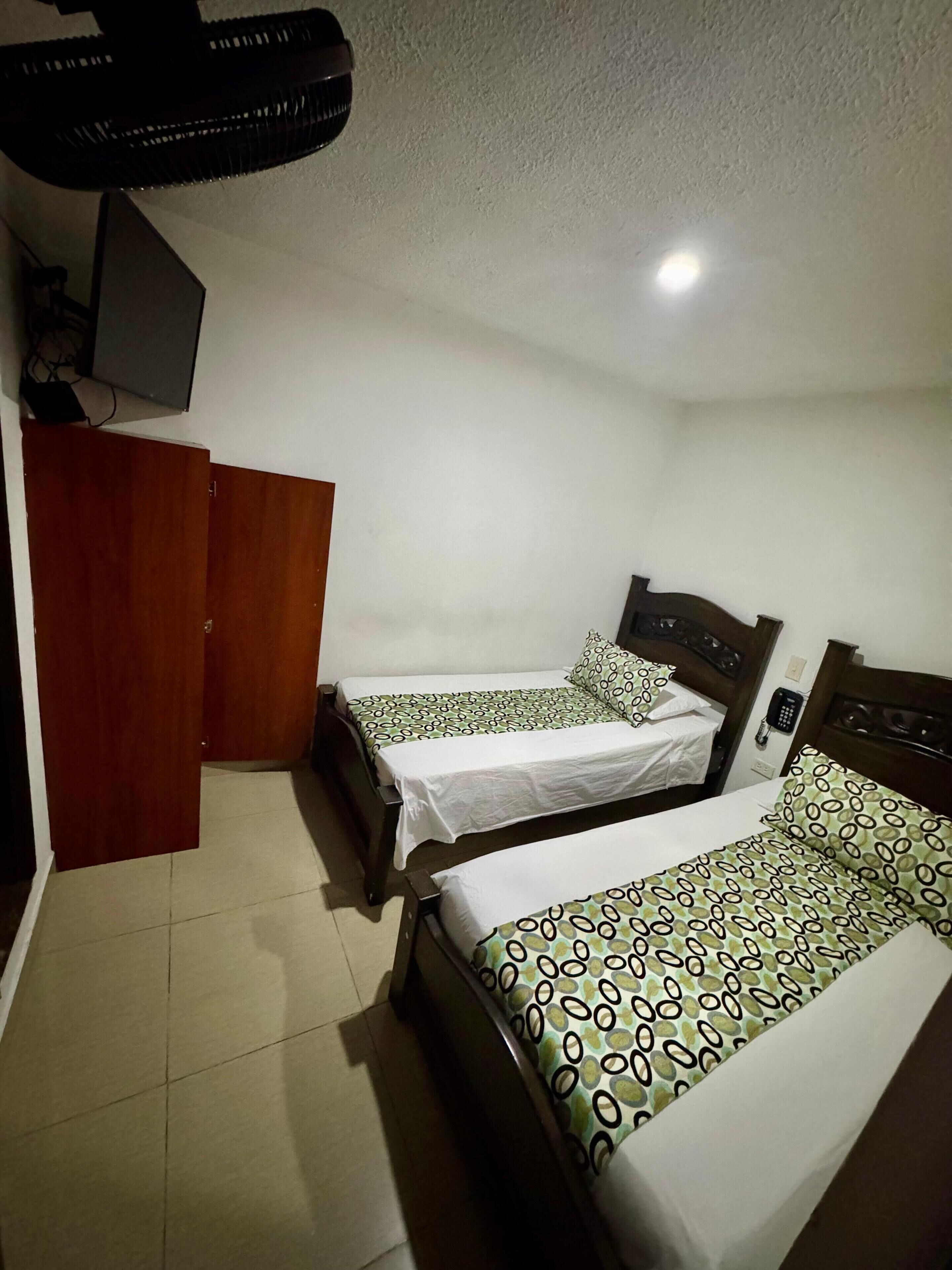 Una habitación con dos camas individuales, un armario y un ventilador de techo.