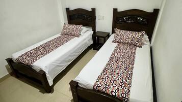 Dos camas individuales con cabeceros de madera y colchas estampadas en una habitación con paredes blancas y suelo de baldosas.