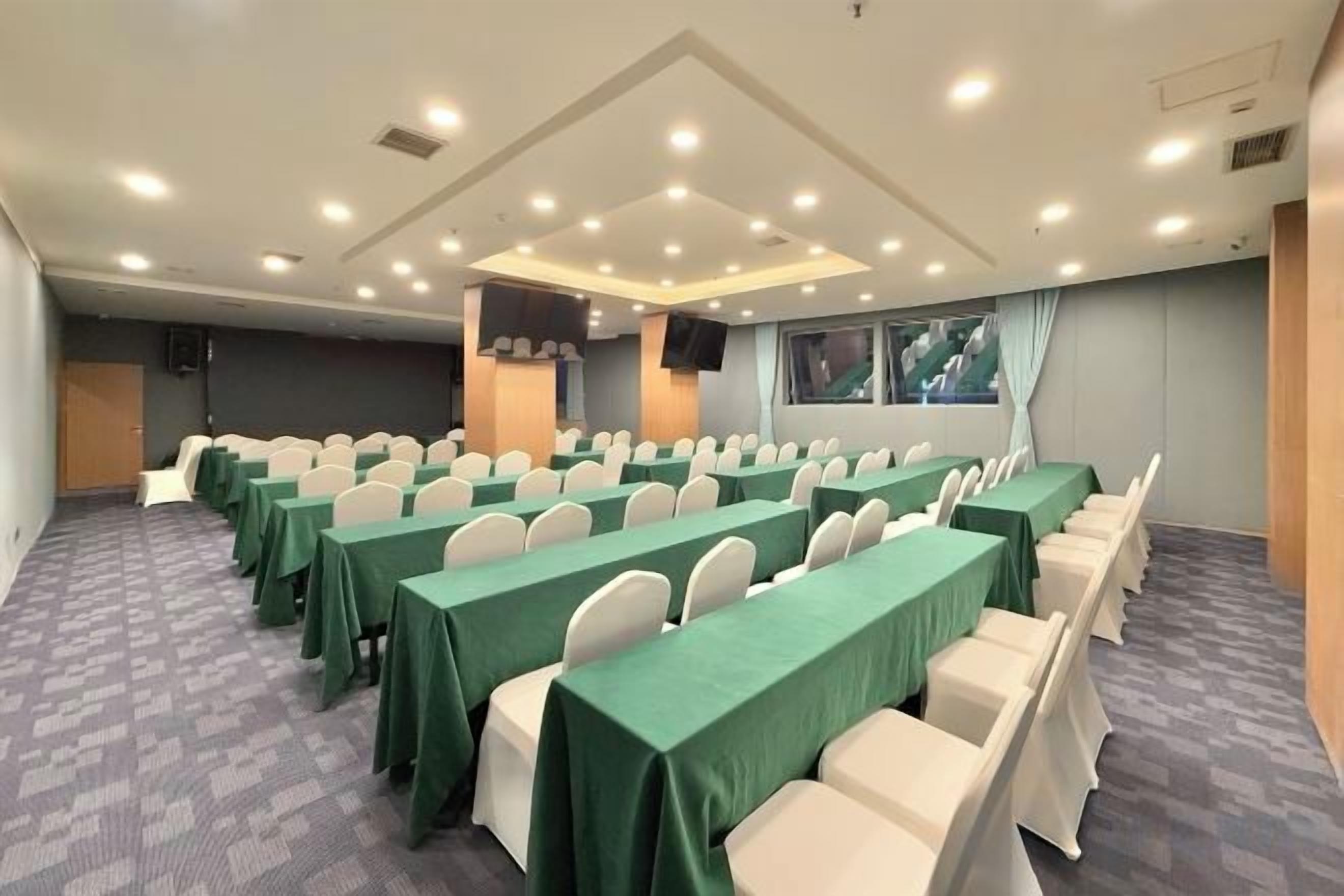 A conference room with rows of tables and chairs, a large screen, and a window with curtains.