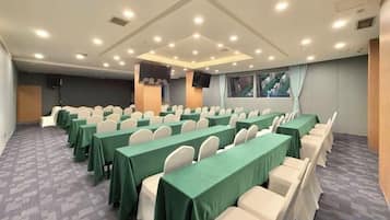 A conference room with rows of tables and chairs, a large screen, and a window with curtains.