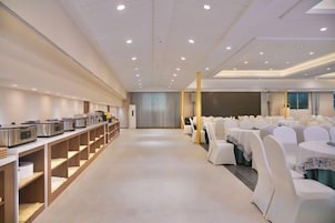 Un salón de conferencias con filas de mesas y sillas, una zona de buffet y un escenario.