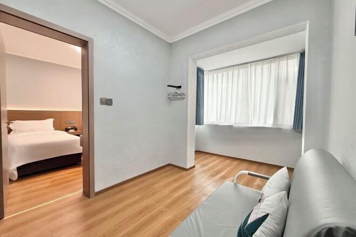 A hotel room with a bed, a seating area with a sofa, a window with curtains, and a wooden floor.