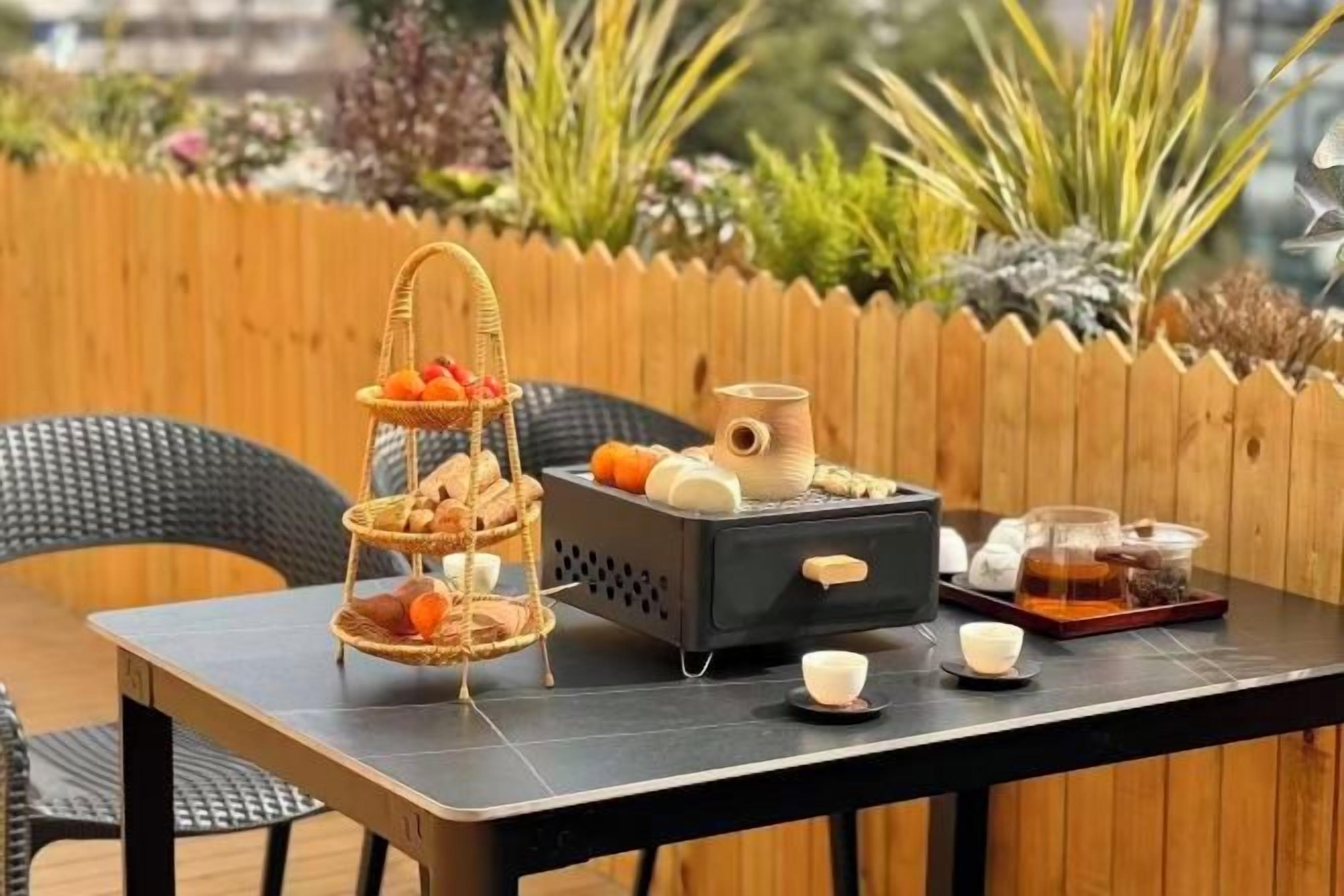 A table set outdoors with a three-tiered fruit and bread basket, a coffee pot, and various condiments.