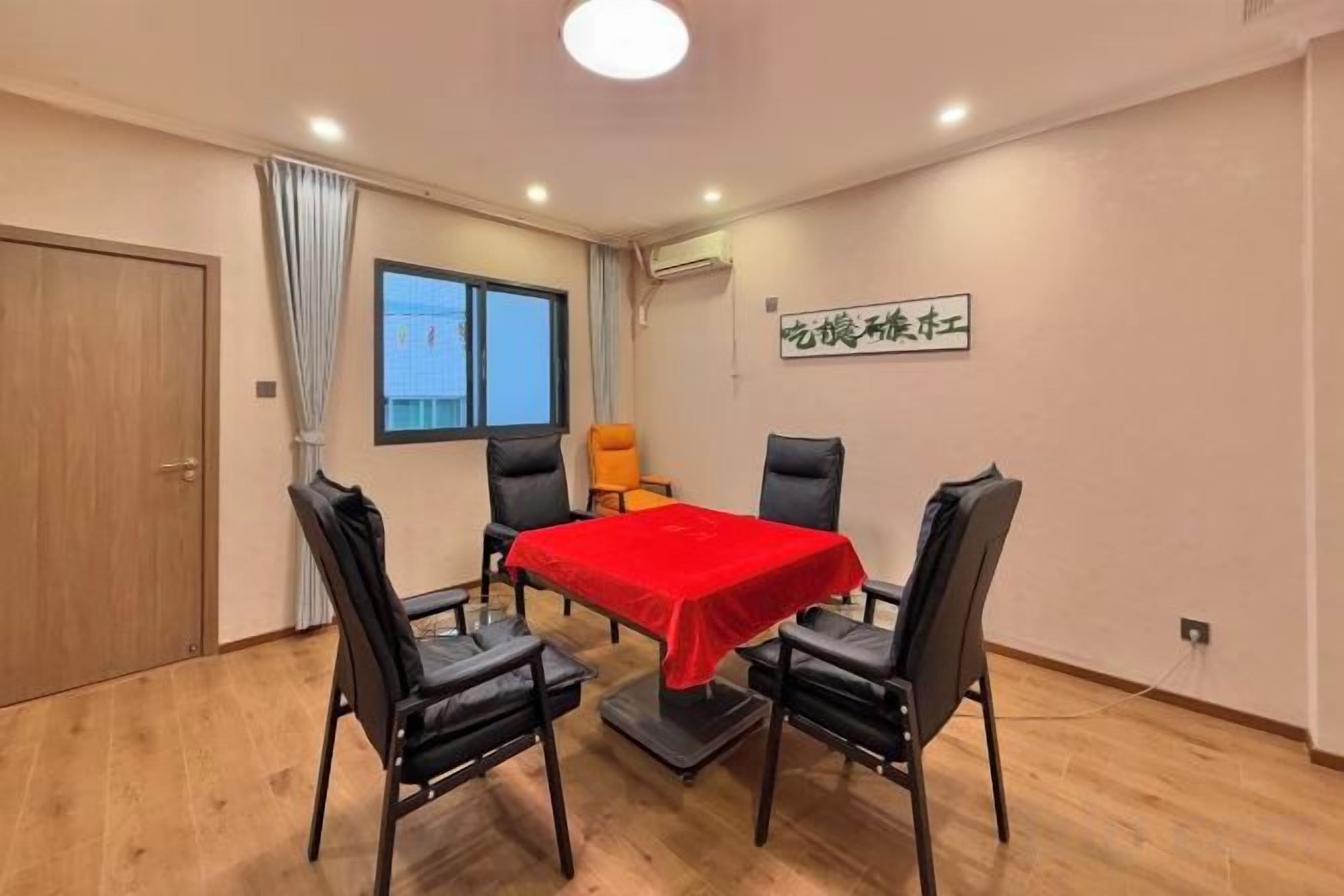 Une pièce avec une table, quatre chaises, une nappe rouge, une fenêtre et une porte.