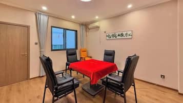 Une pièce avec une table, quatre chaises, une nappe rouge, une fenêtre et une porte.