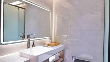 A modern bathroom with a large mirror, a white sink, and a wooden tray.