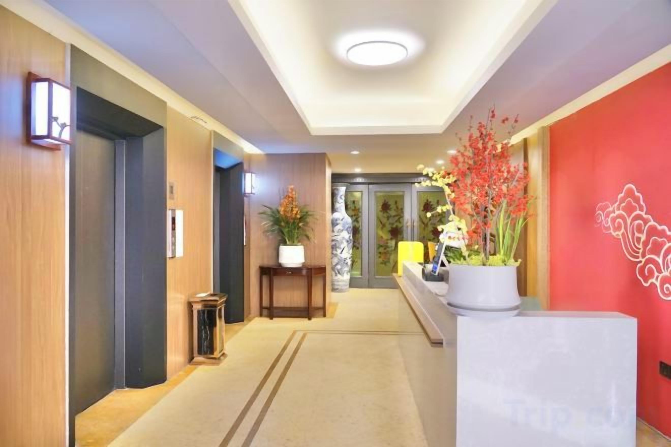 A hotel lobby with a reception desk, a plant, and a red wall.