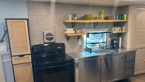 Een moderne keuken met een roestvrijstalen fornuis, een inbouwoven en een spoelbak. Er zijn houten keukenkastjes en een raam boven de spoelbak.