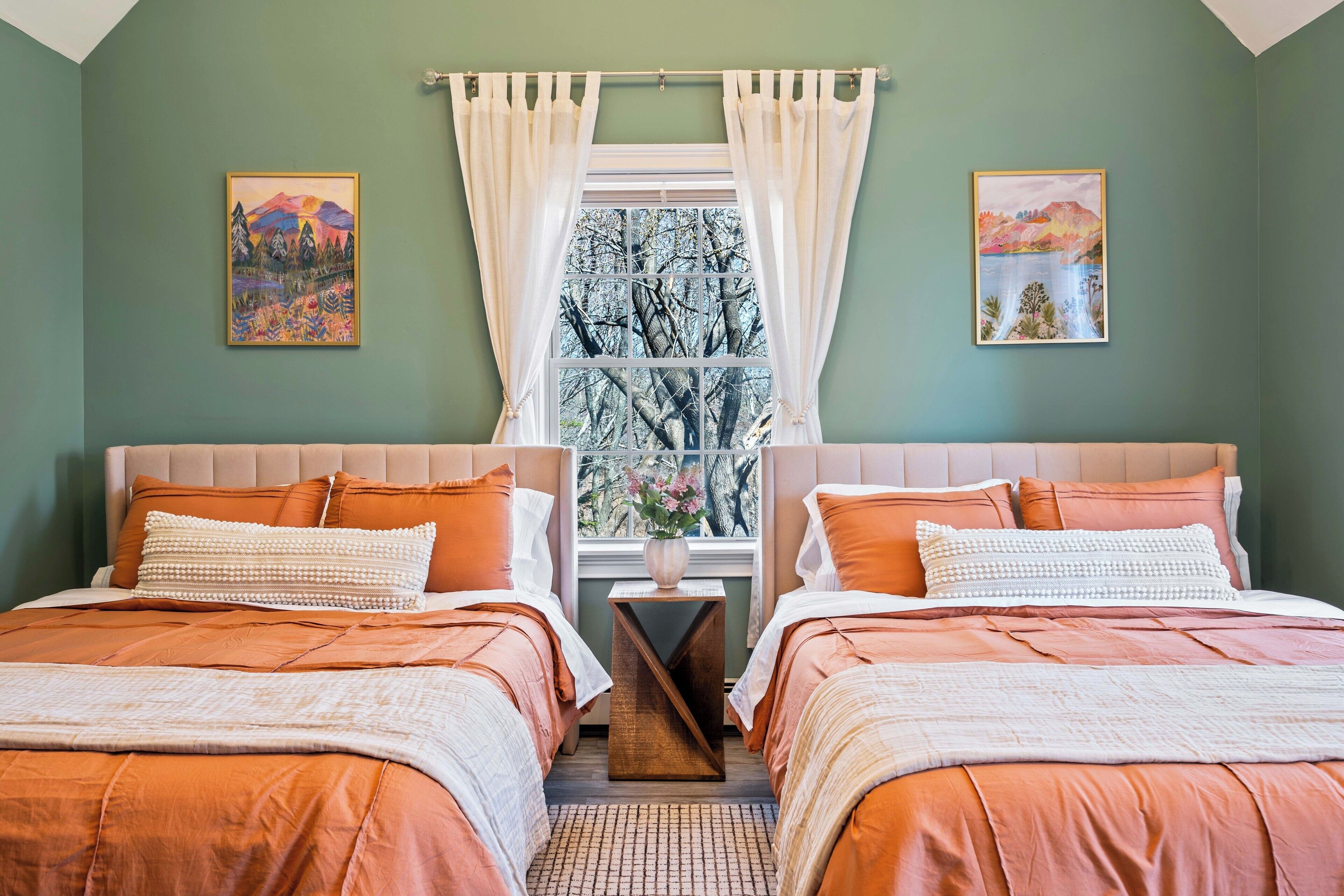 Een slaapkamer met twee bedden, een raam met gordijnen, en twee schilderijen aan de muur.