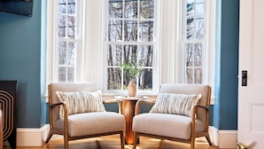 Una habitación con dos sillones orientados hacia un ventanal que ofrece vistas a árboles y un florero sobre una mesa de madera.