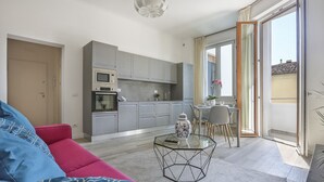 A modern apartment with a living area featuring a glass coffee table, a red sofa, and a kitchen with grey cabinets and a microwave. - Modern Comfort in Florence (Firenze)