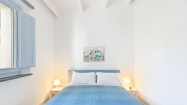 Une chambre à coucher comprenant un lit, deux tables de chevet avec des lampes, une fenêtre et une œuvre d’art accrochée au mur.