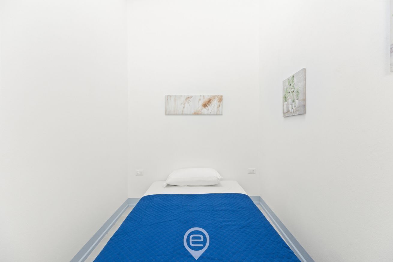 Een minimalistisch hotelkamer met een enkel bed, een blauwe spreidek en twee kunstwerken aan de muur.